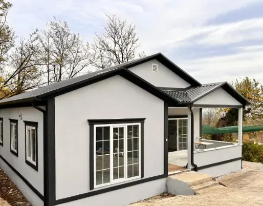 Antrasit çerçeveli gri ev, beyaz Fransız pencereler, yanında üstü kapalı veranda, arkada ağaçlar
