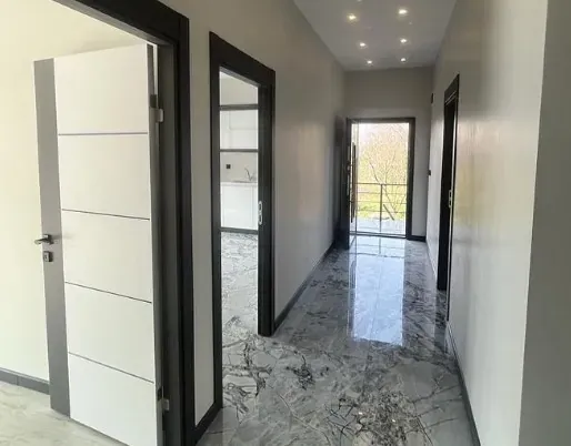 Mermer zeminli giriş holü, beyaz kapılar, antrasit kasalar ve tavanda gömme spotlar, sonunda bahçeye açılan kapı